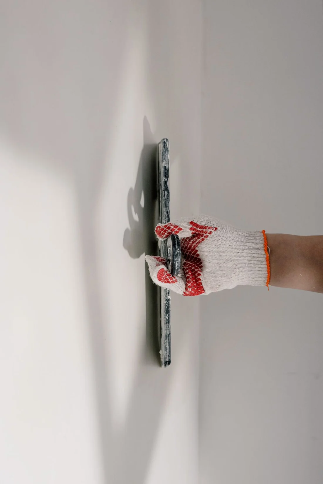 A plasterer in a t-shirt smoothing a wall with a float during a room refurbishment