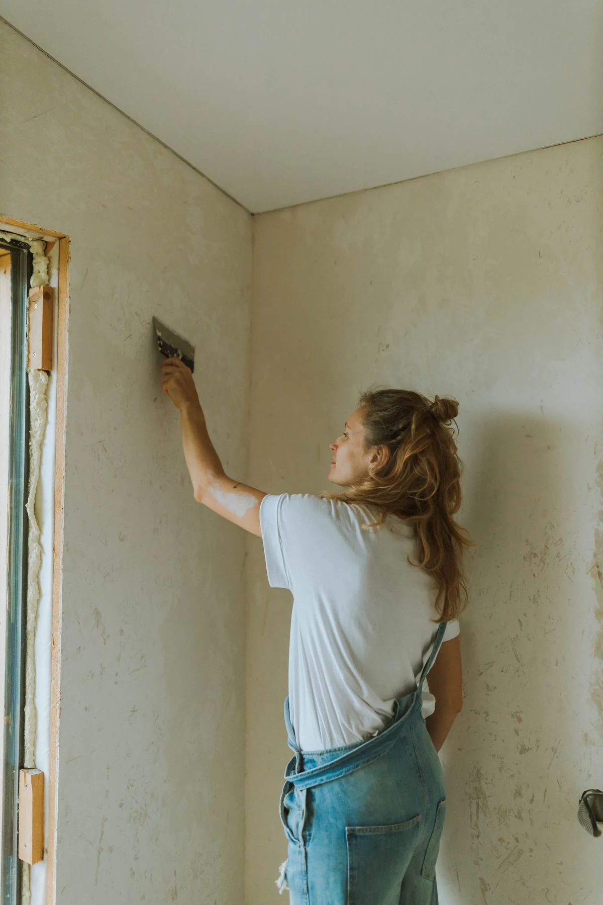 A plasterer skimming the corner of a room, working the fresh plaster smooth beside a window reveal