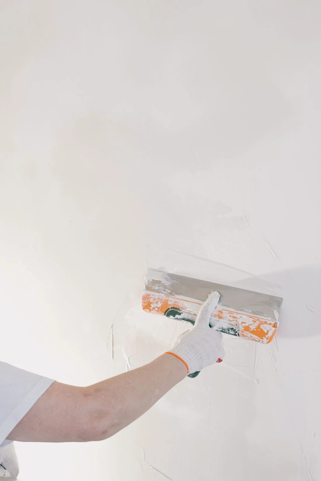 Close-up of a float skimming a fresh coat of plaster smooth across a ceiling